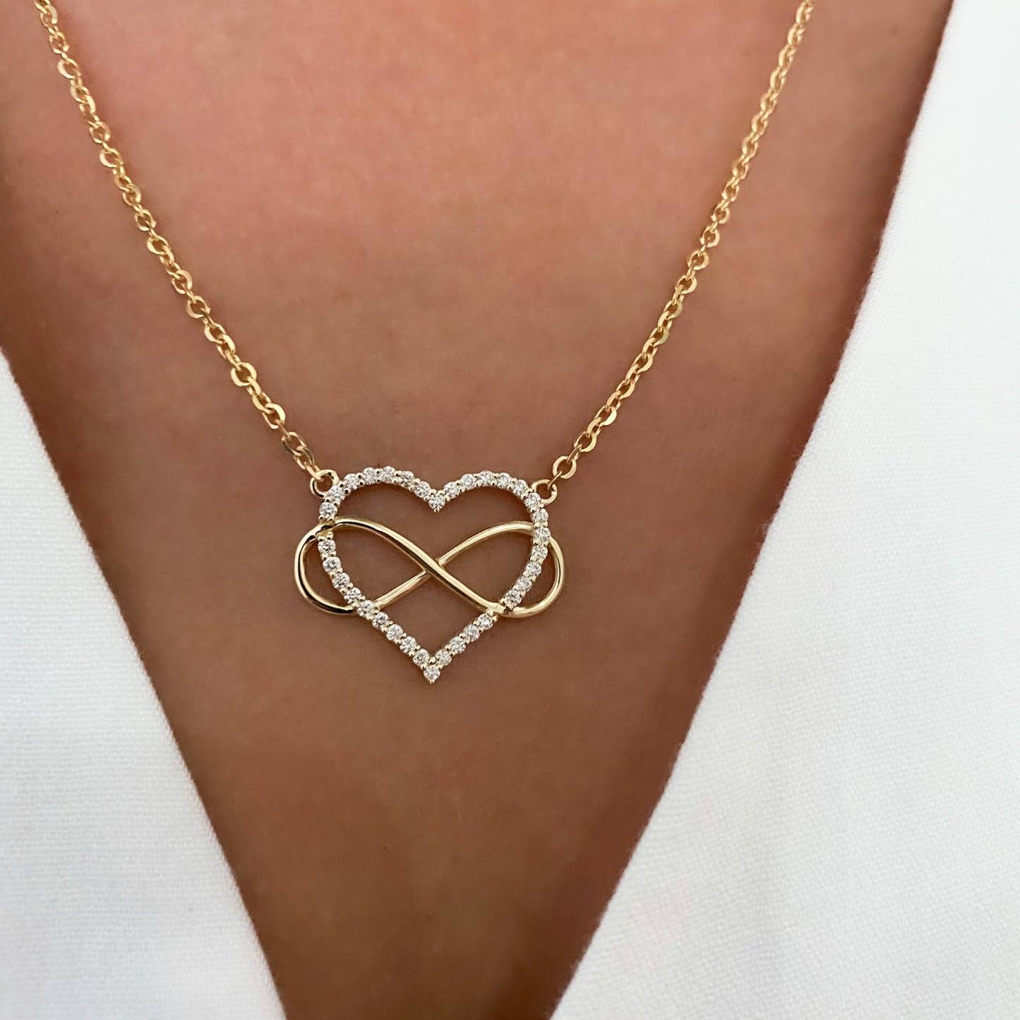 A heart-shaped pendant necklace with a diamonds and gold infinity symbol, attached to a yellow gold chain, displayed on womens neck