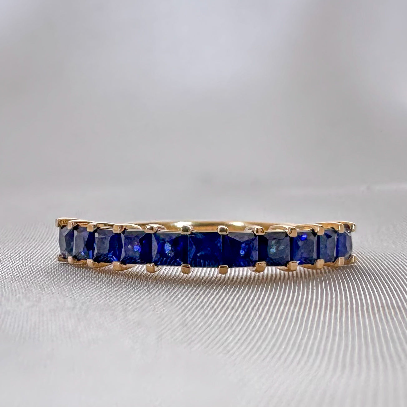 A princess cut natural sapphires eternity ring made from 14K gold, with a series of blue sapphire stones set in a gold band.