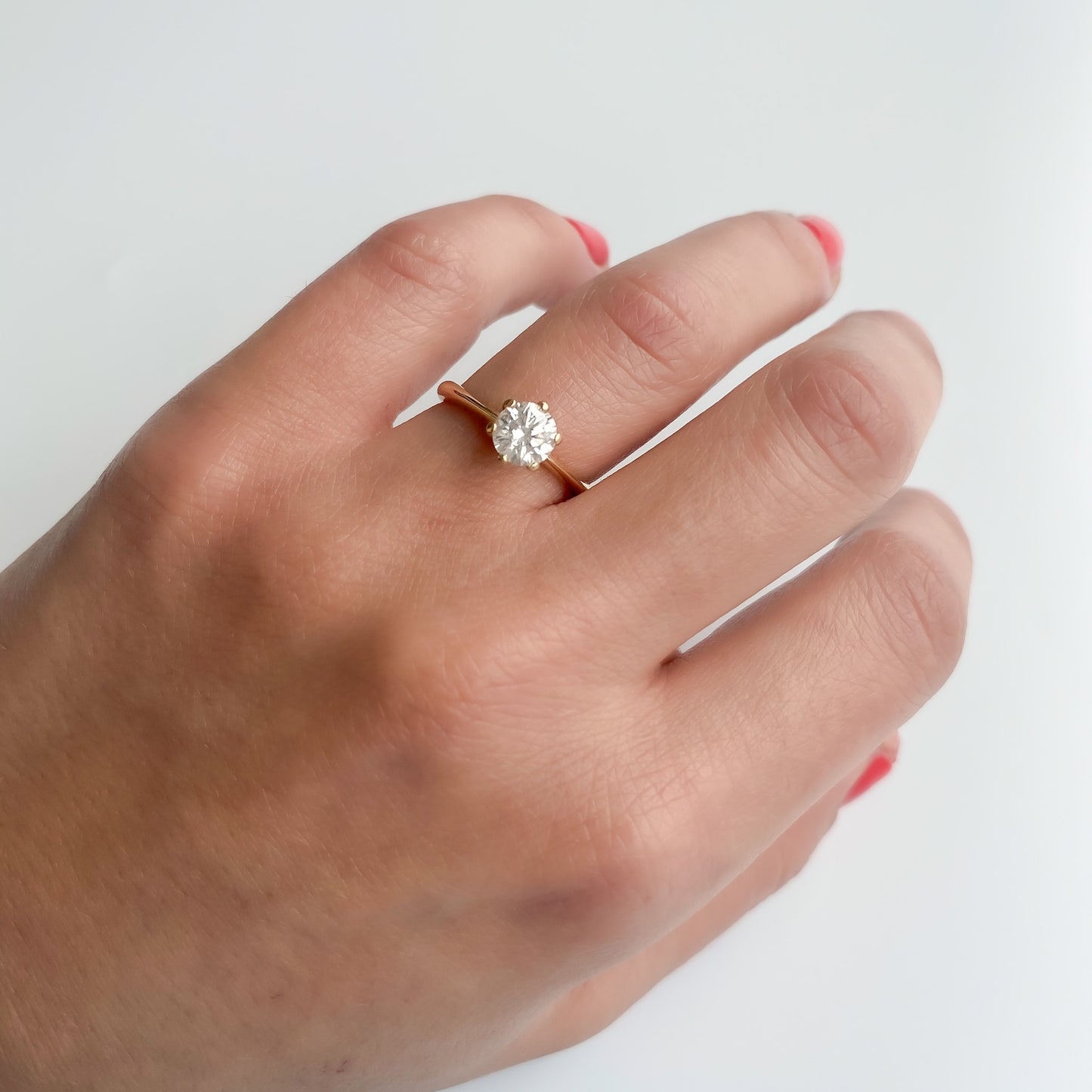 A hand wearing a 14K yellow gold solitaire diamond engagement ring with a clear and sparkling diamond set in a classic six-prong design.