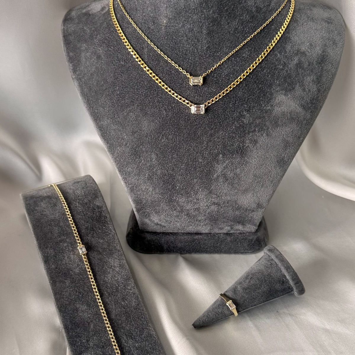 Emerald cut diamond curb chain choker shown with a matching ring and bracelet on gray stands