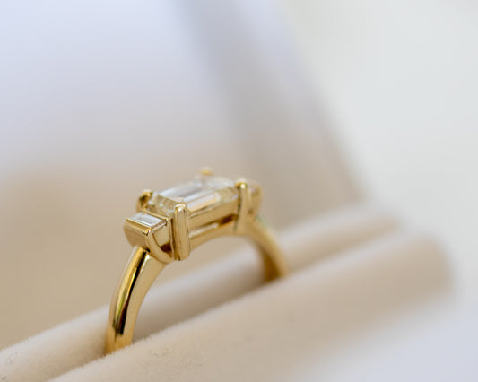Emerald cut diamond trilogy ring in 14K yellow gold on white surface