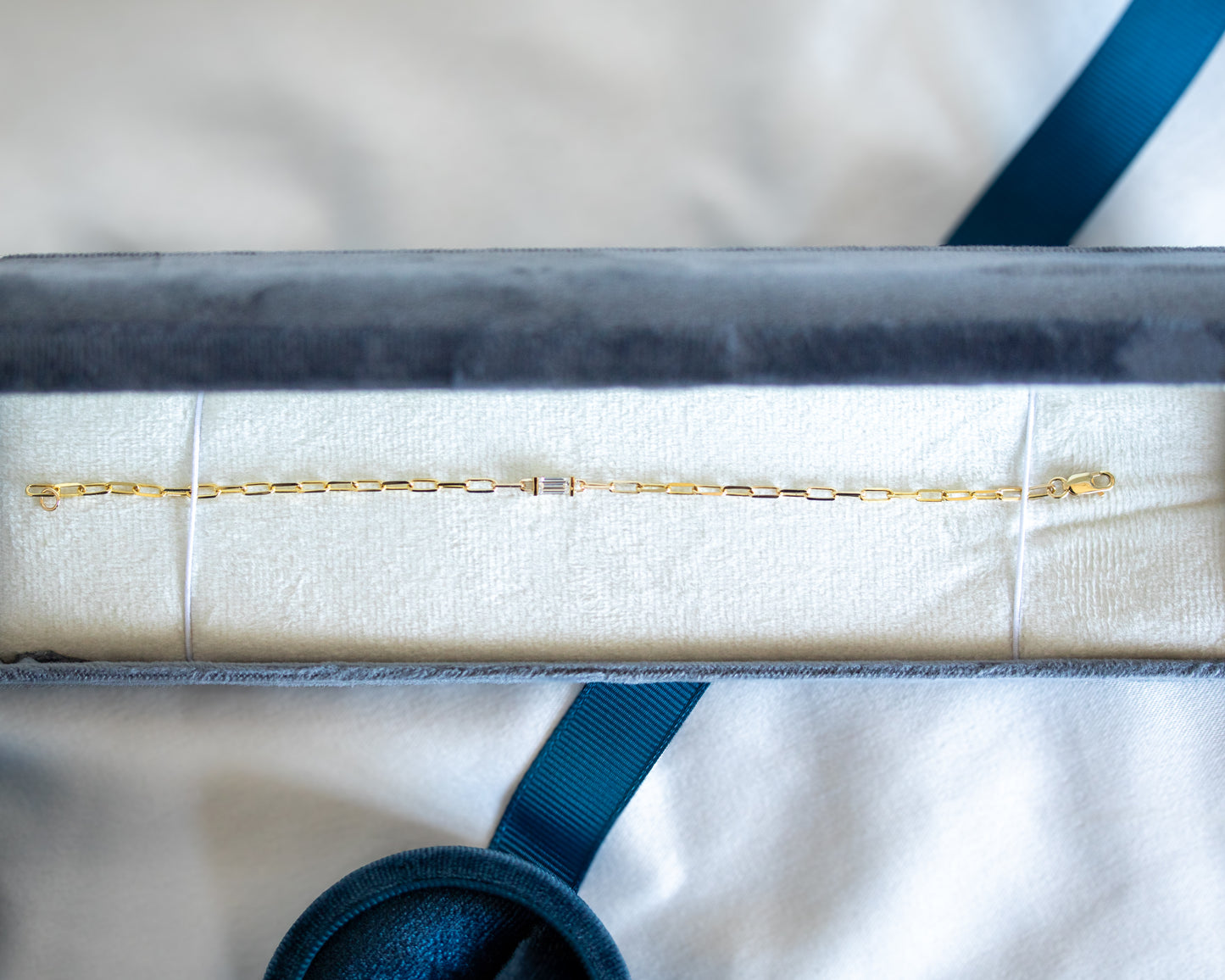 Gold bracelet with baguette cut diamond on a white cushion with a blue ribbon in the background