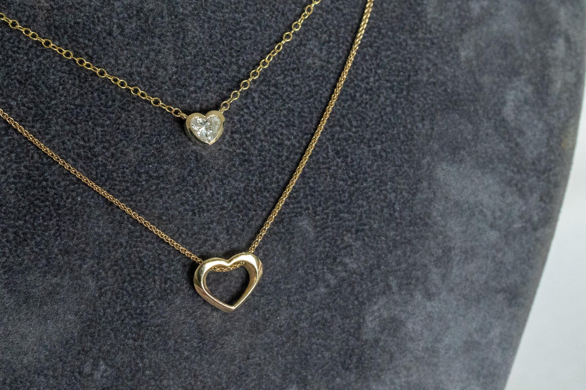 Heart shape diamond bezel necklace layered with a 14K yellow gold open heart necklace on a spiga chain
