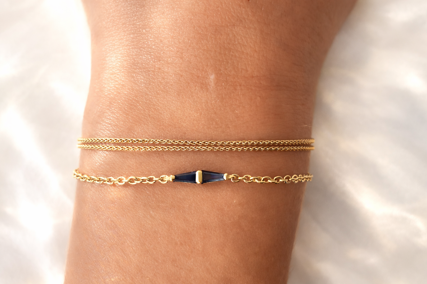 Layered 14K gold bracelets featuring a geometric blue sapphire bracelet worn on the wrist