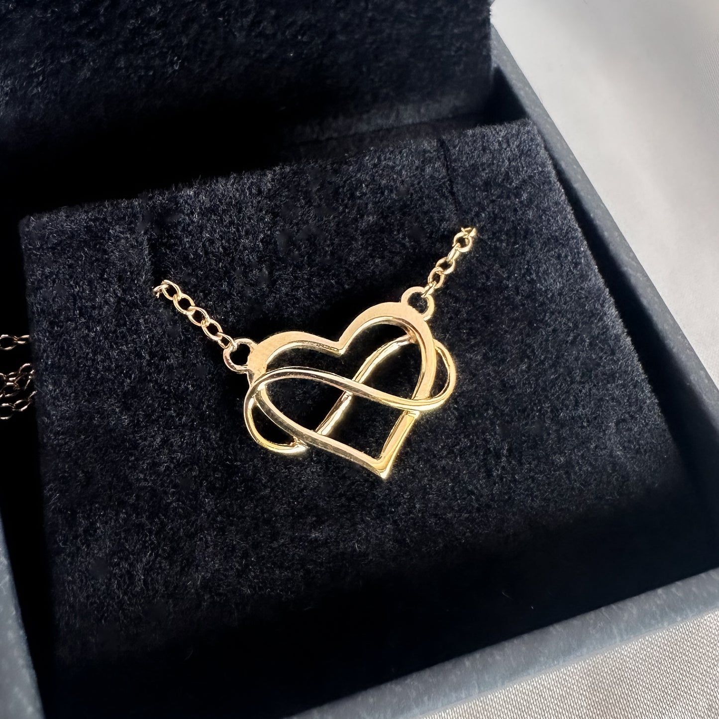 close up yellow gold heart and infinity symbol pendant and chain in black velvet box