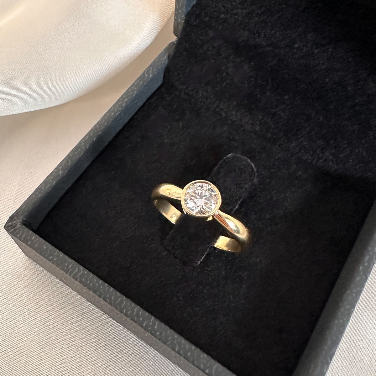 Close-up of a round diamond bezel solitaire ring in a black velvet box