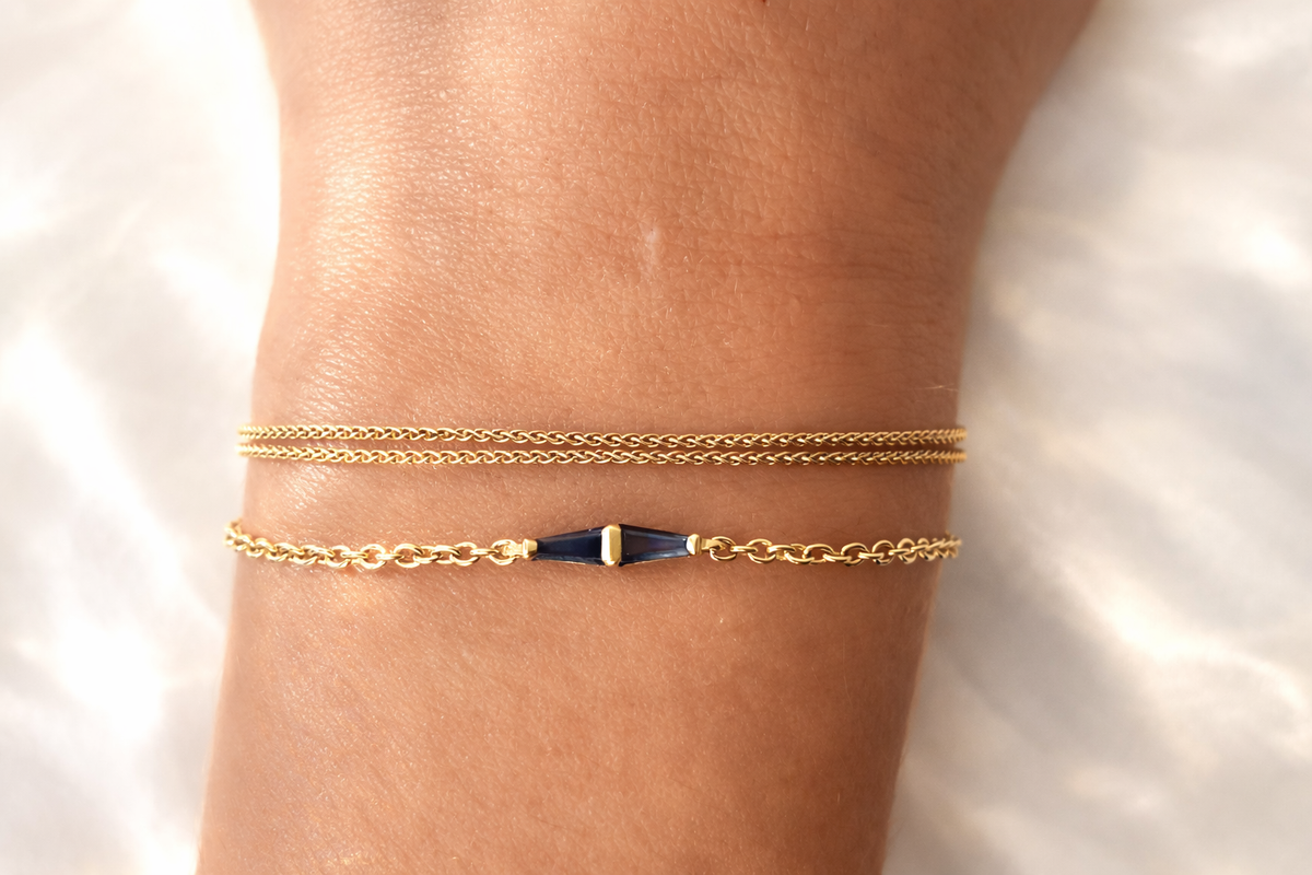Tapered baguette blue sapphire bracelet worn on the wrist with a second gold bracelet