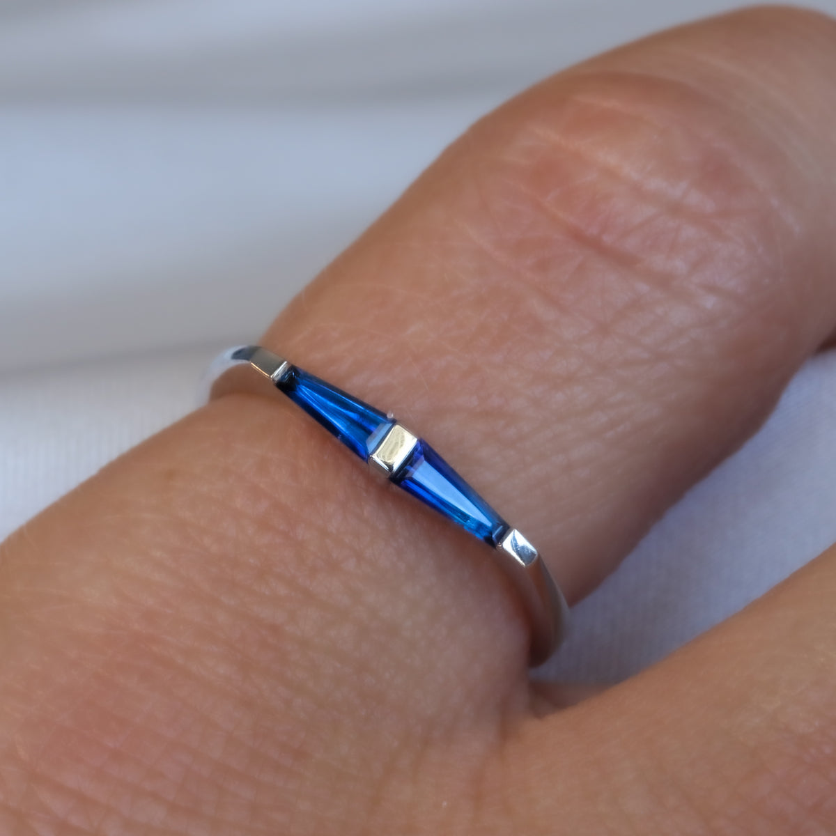 14K white gold ring with two tapered baguette blue sapphires worn on a finger