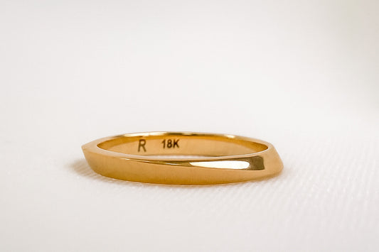 Close-up of a polished 18K yellow gold ring engraved with “R 18K” inside the band, photographed on a soft white background under gentle natural light — highlighting the craftsmanship and warm tone of fine gold jewelry.