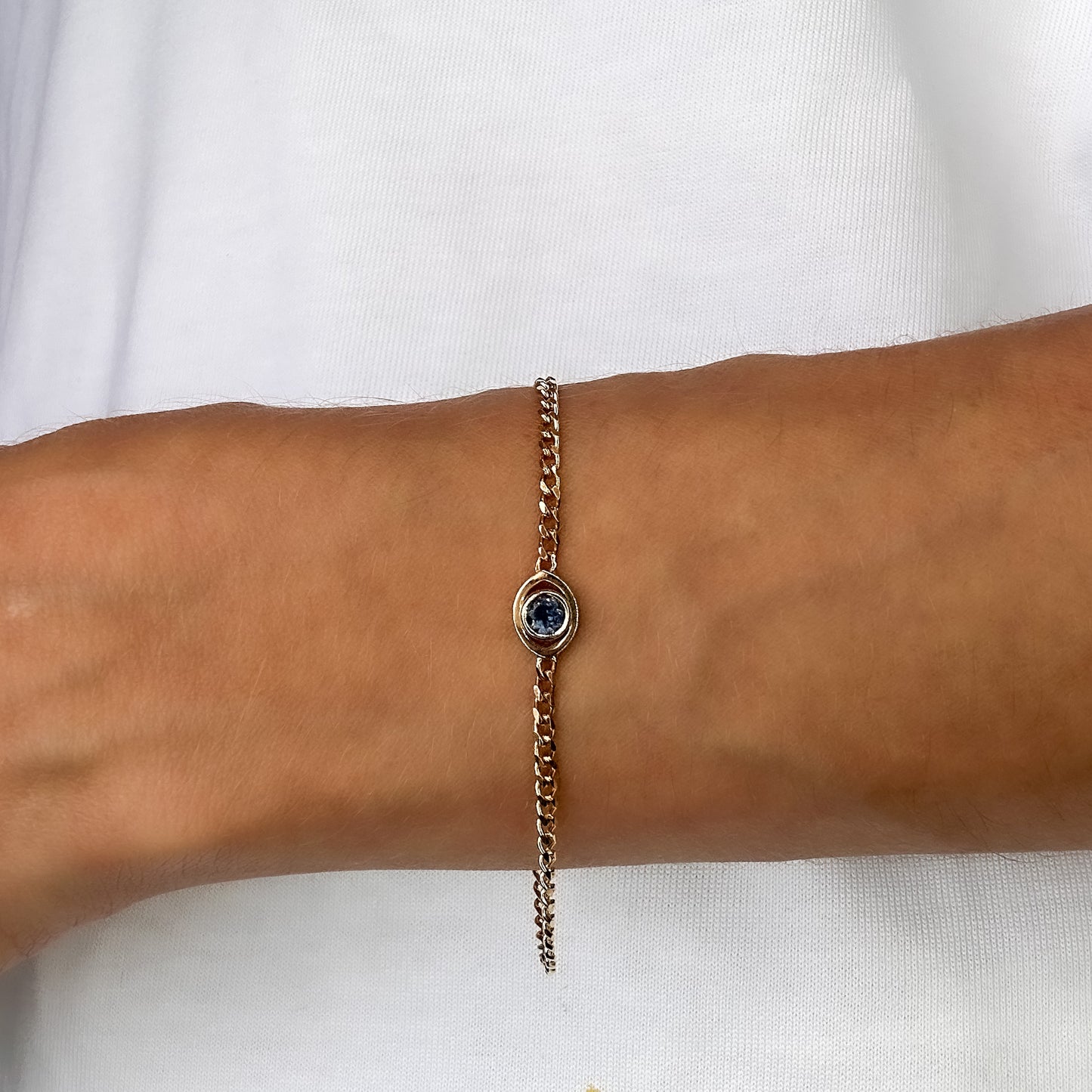 A person wearing a gold curb chain bracelet with a blue sapphire set in a evil eye centerpiece on their wrist.