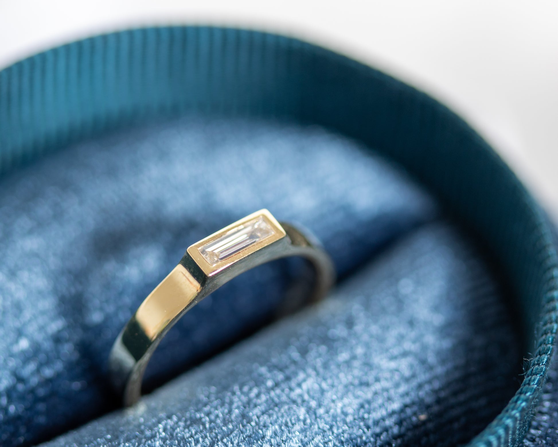 Close-up of bezel-set baguette diamond in 14K gold ring in jewelry box