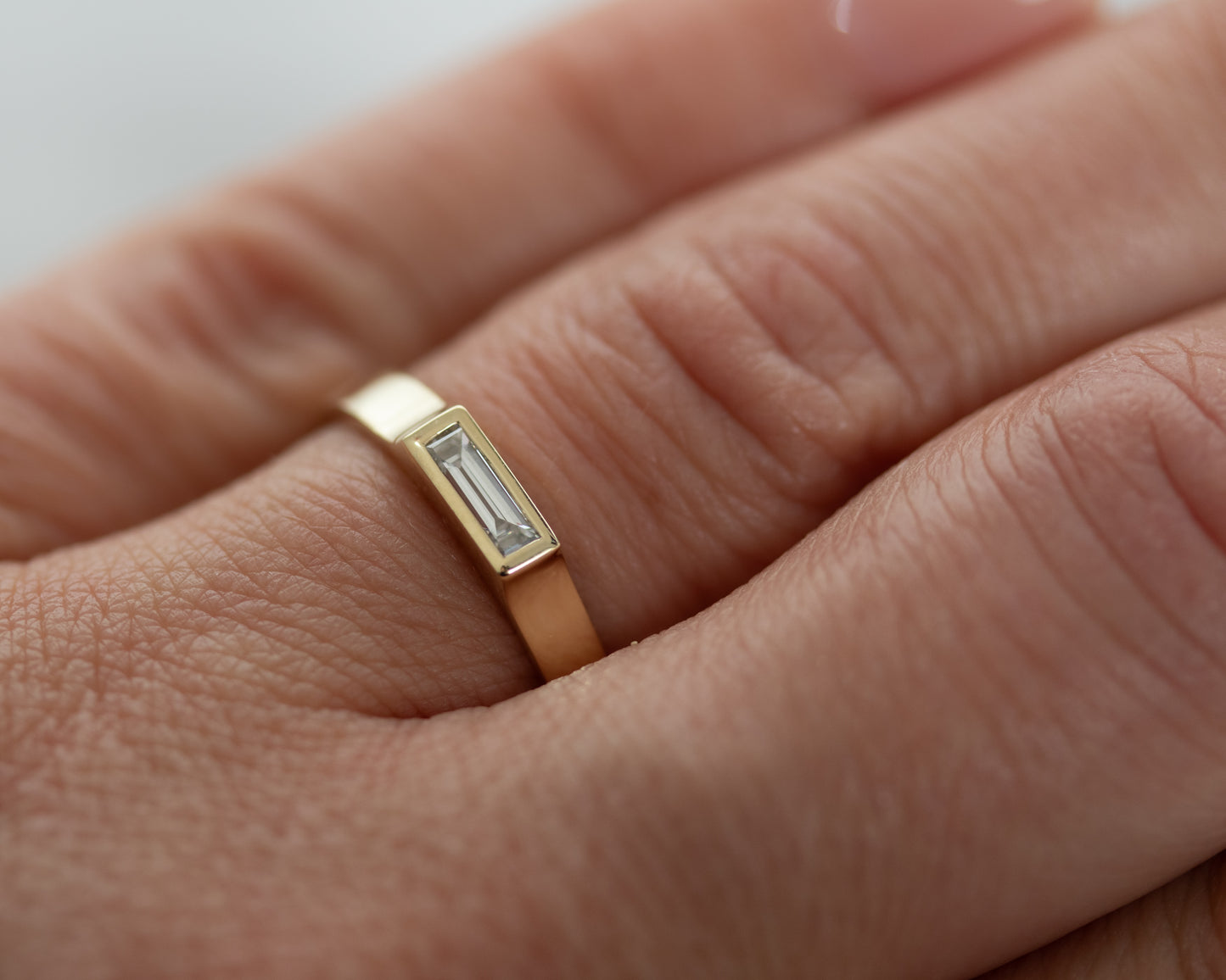 14K yellow gold bezel-set baguette diamond ring worn on finger