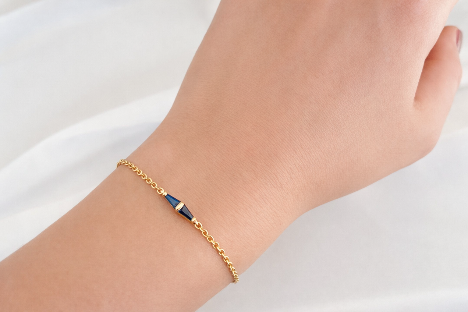 Minimal 14K gold bracelet with a geometric blue sapphire detail worn on the wrist