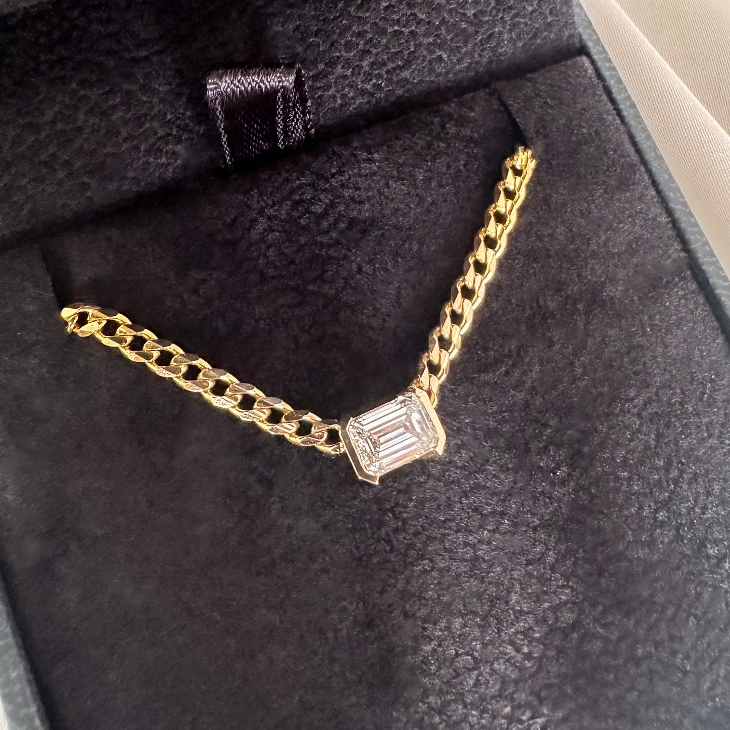A 14K gold diamond solitaire necklace with an emerald cut natural diamond pendant in a black velvet box