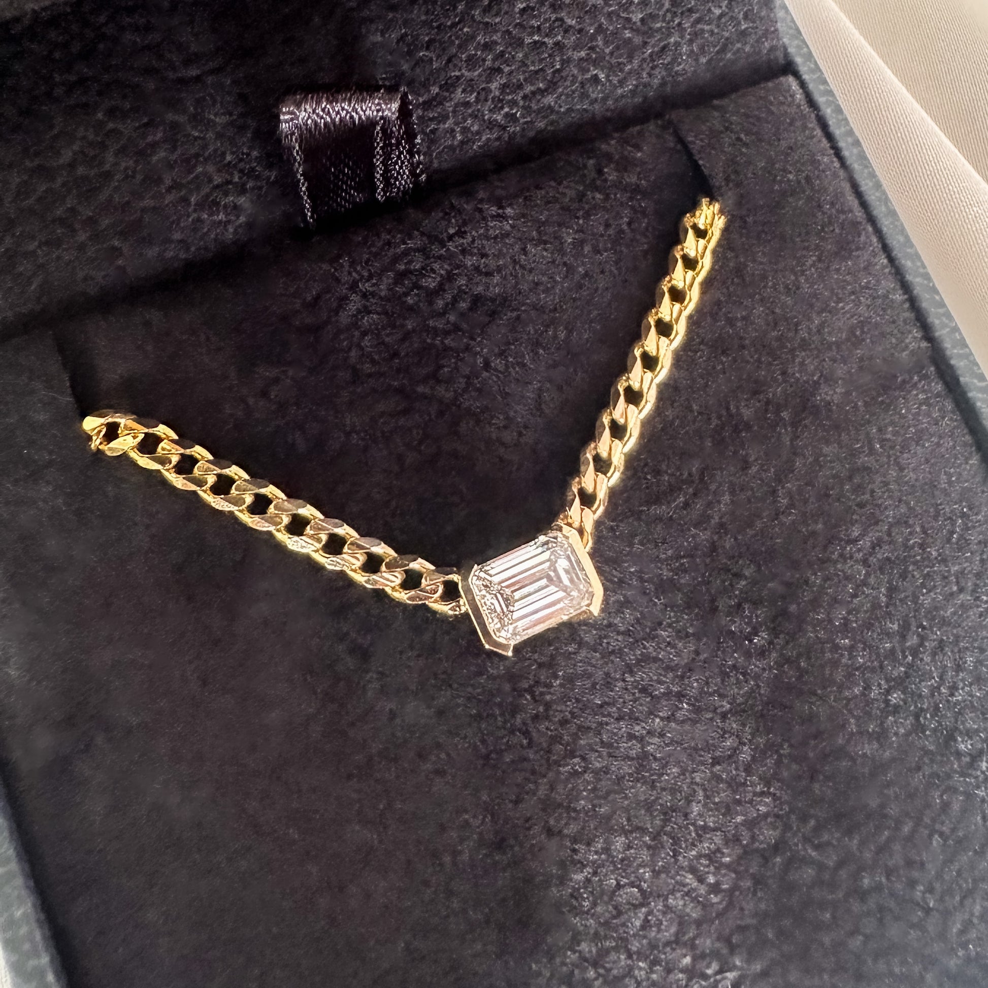 A 14K gold diamond solitaire necklace with an emerald cut natural diamond pendant in a black velvet box
