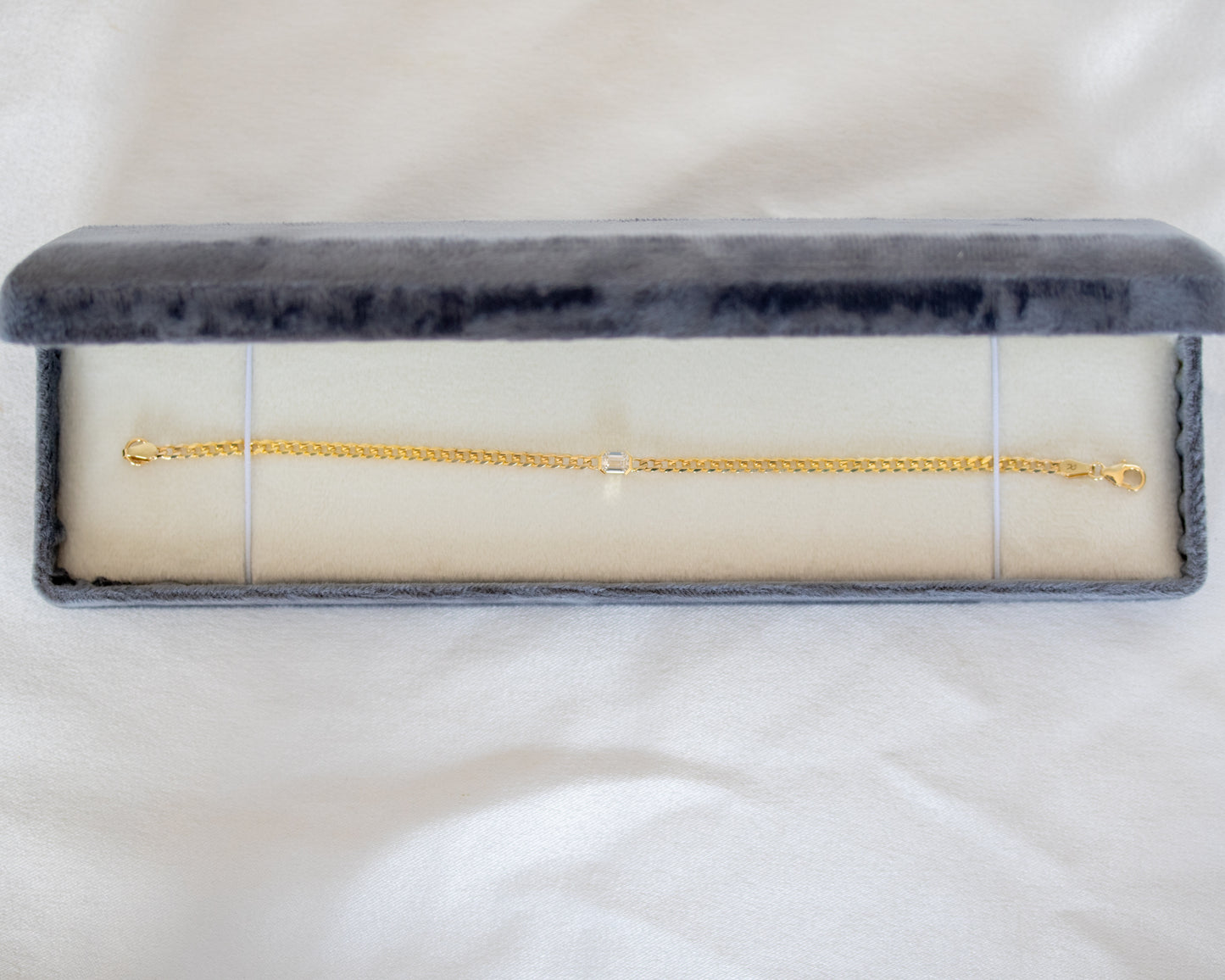 Gold chain with emerald cut diamond in a gray velvet box on a white background