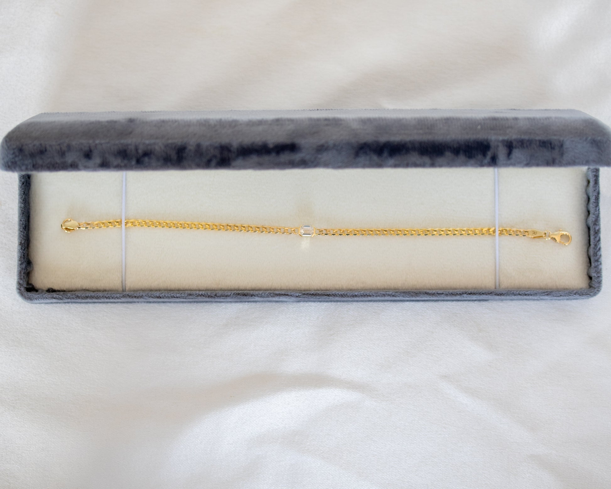 Gold chain with emerald cut diamond in a gray velvet box on a white background