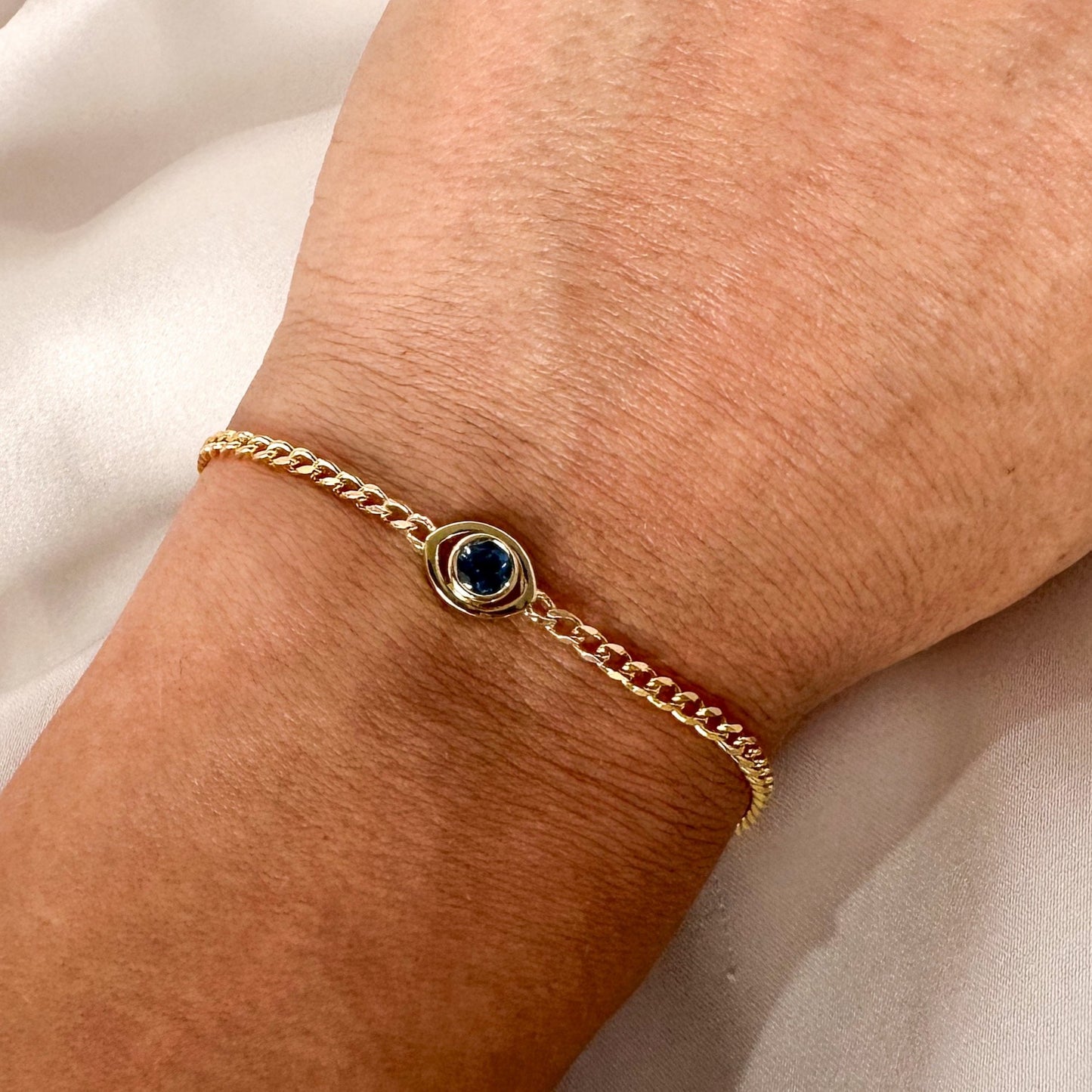  gold curb chain bracelet with a blue sapphire set in a evil eye centerpiece shown on person's wrist.