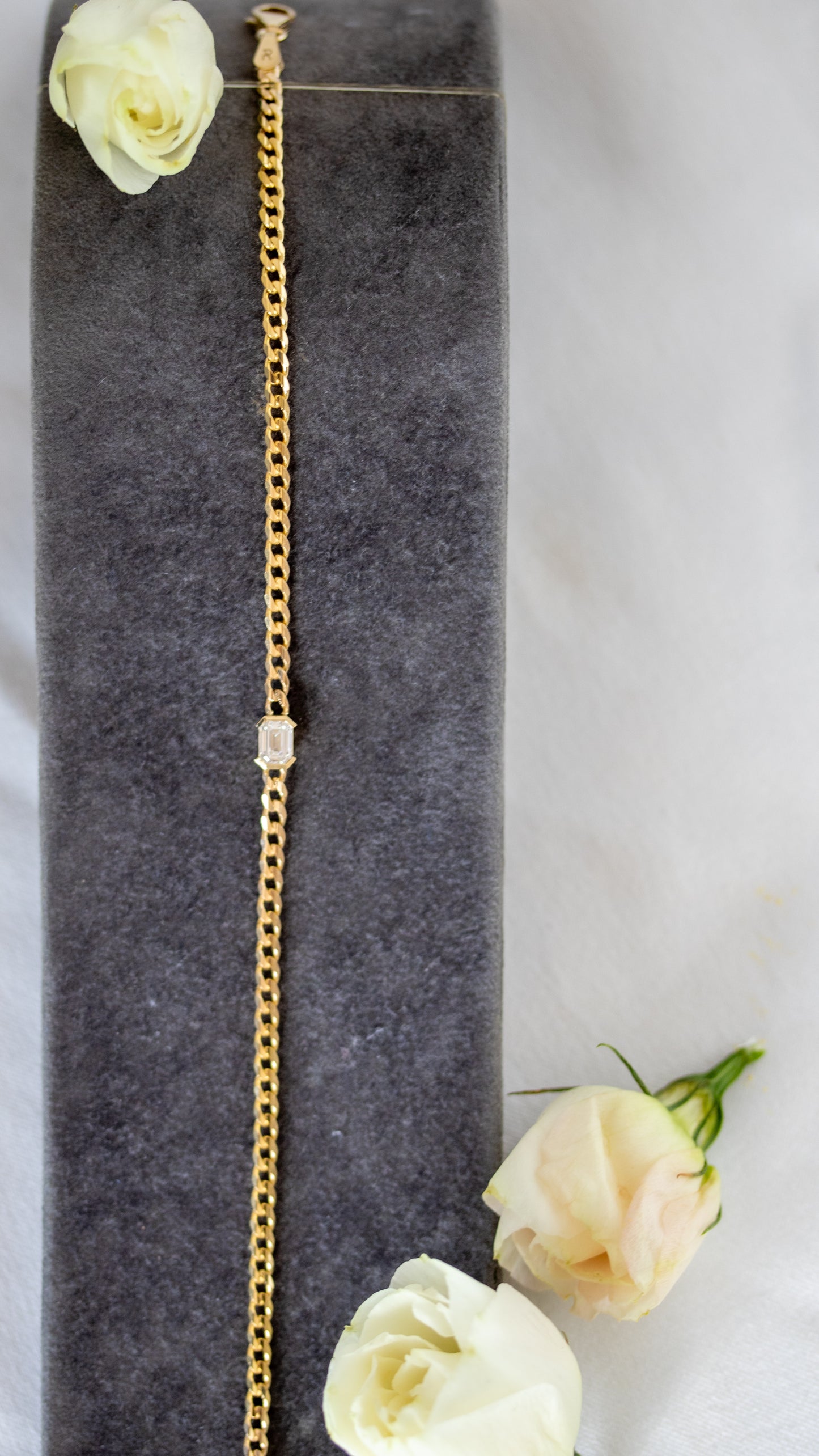 Gold bracelet with an emerald cut diamond on a gray surface