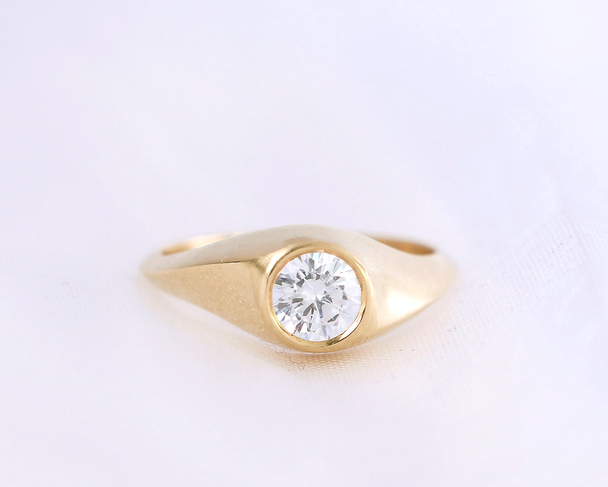 Elegant 14K gold diamond signet ring with round brilliant-cut stone, minimalist handcrafted fine jewelry on soft cream background.