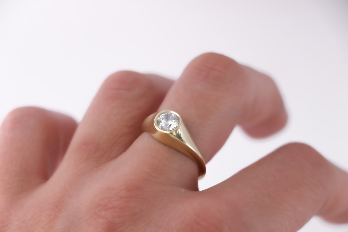 Side view of 14K gold diamond signet ring on hand, minimalist handcrafted fine jewelry with round brilliant-cut stone and smooth polished band.