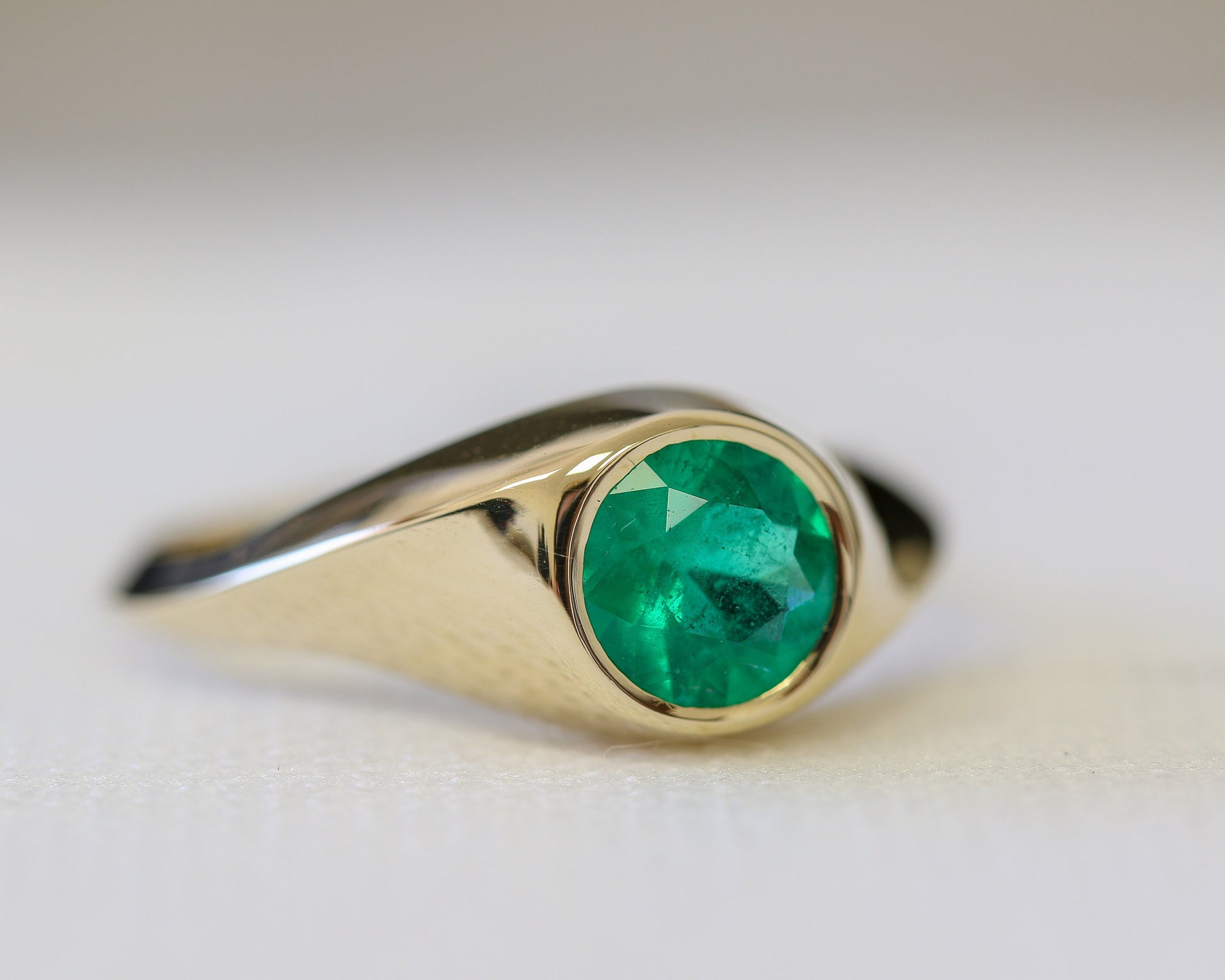 Close-up of 14K gold signet ring featuring vivid green natural emerald gemstone, handcrafted fine jewelry with polished finish.