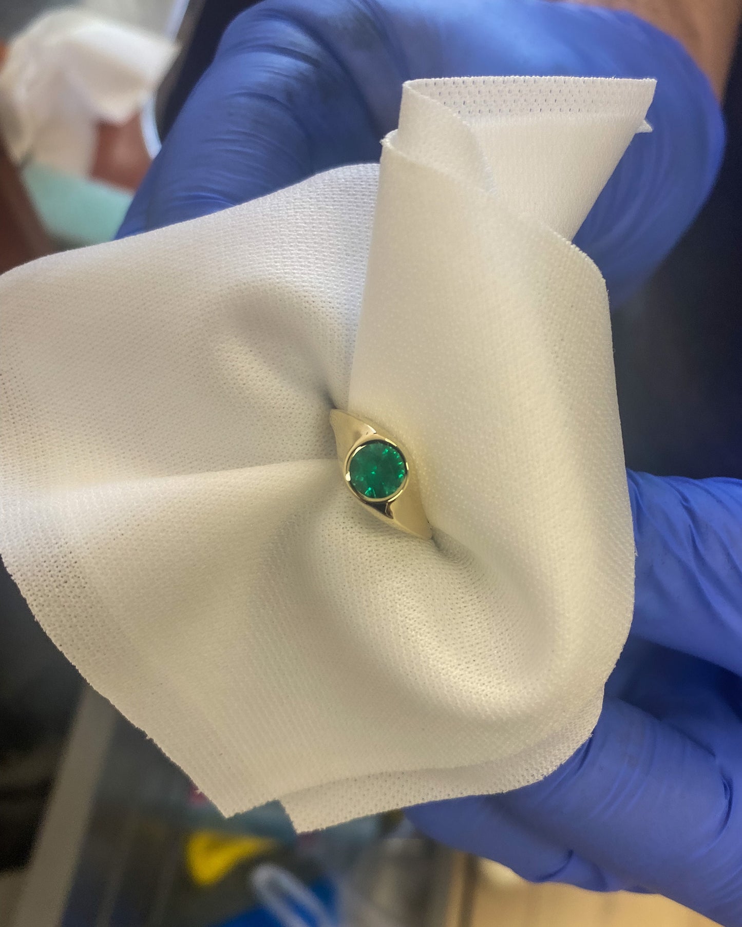 14K gold emerald signet ring during polishing process, held with white cloth by jeweler wearing gloves, showcasing handcrafted fine jewelry craftsmanship.