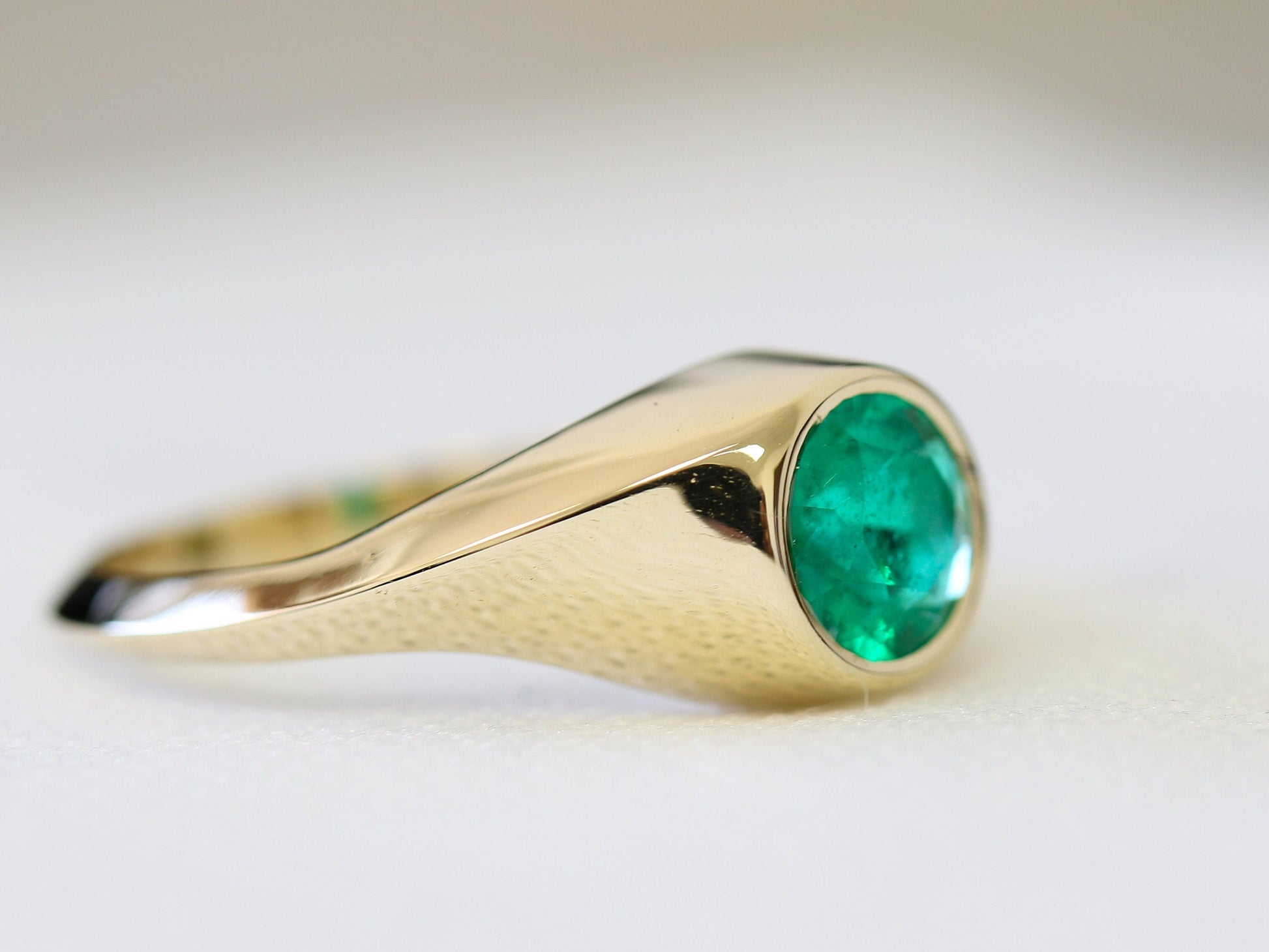 Side view of 14K gold signet ring with round natural emerald gemstone, handcrafted fine jewelry showcasing smooth polished gold band.