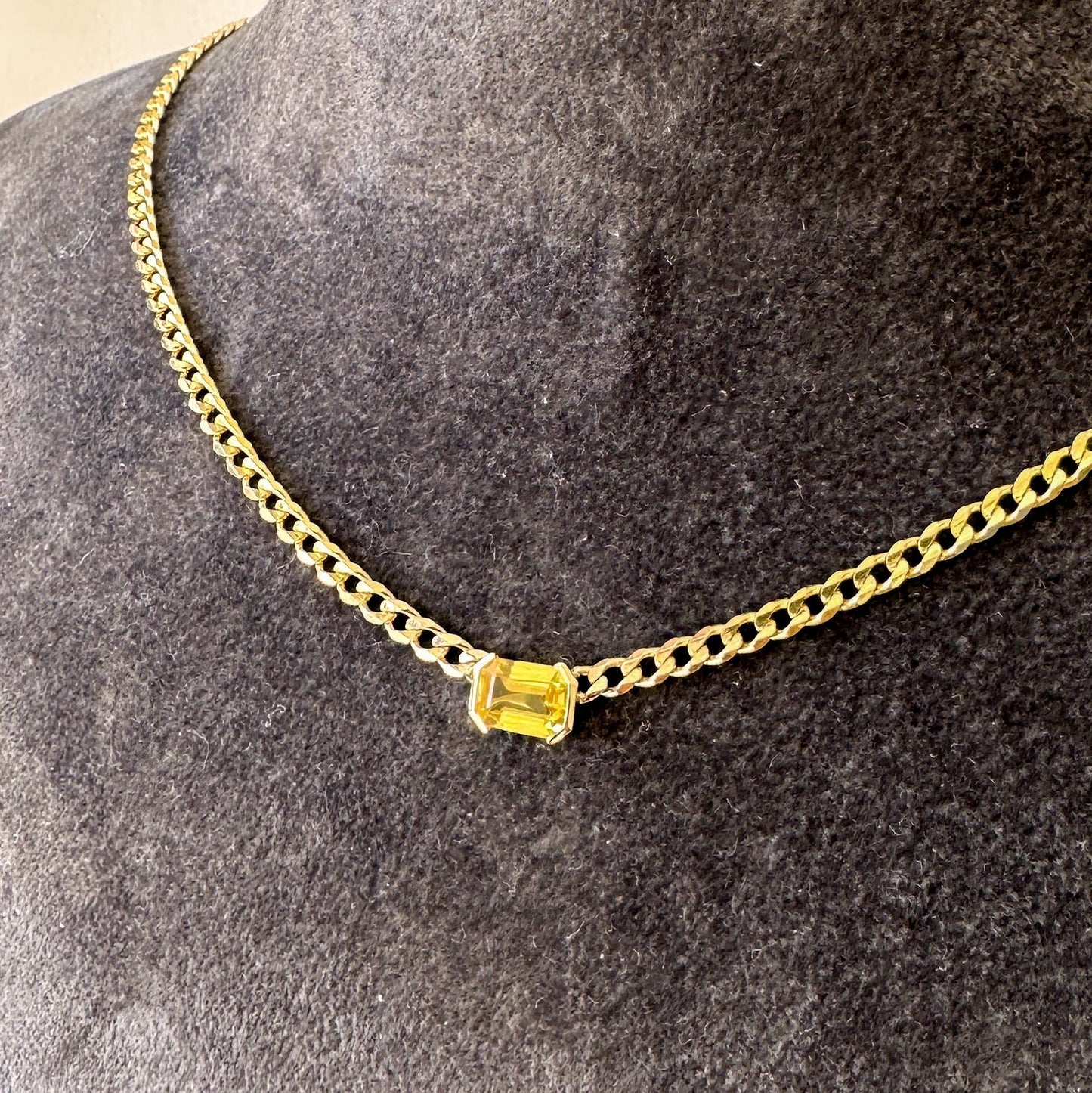 A 14K gold yellow sapphire solitaire necklace with an emerald cut natural diamond pendant on a gray textured jewelry torso