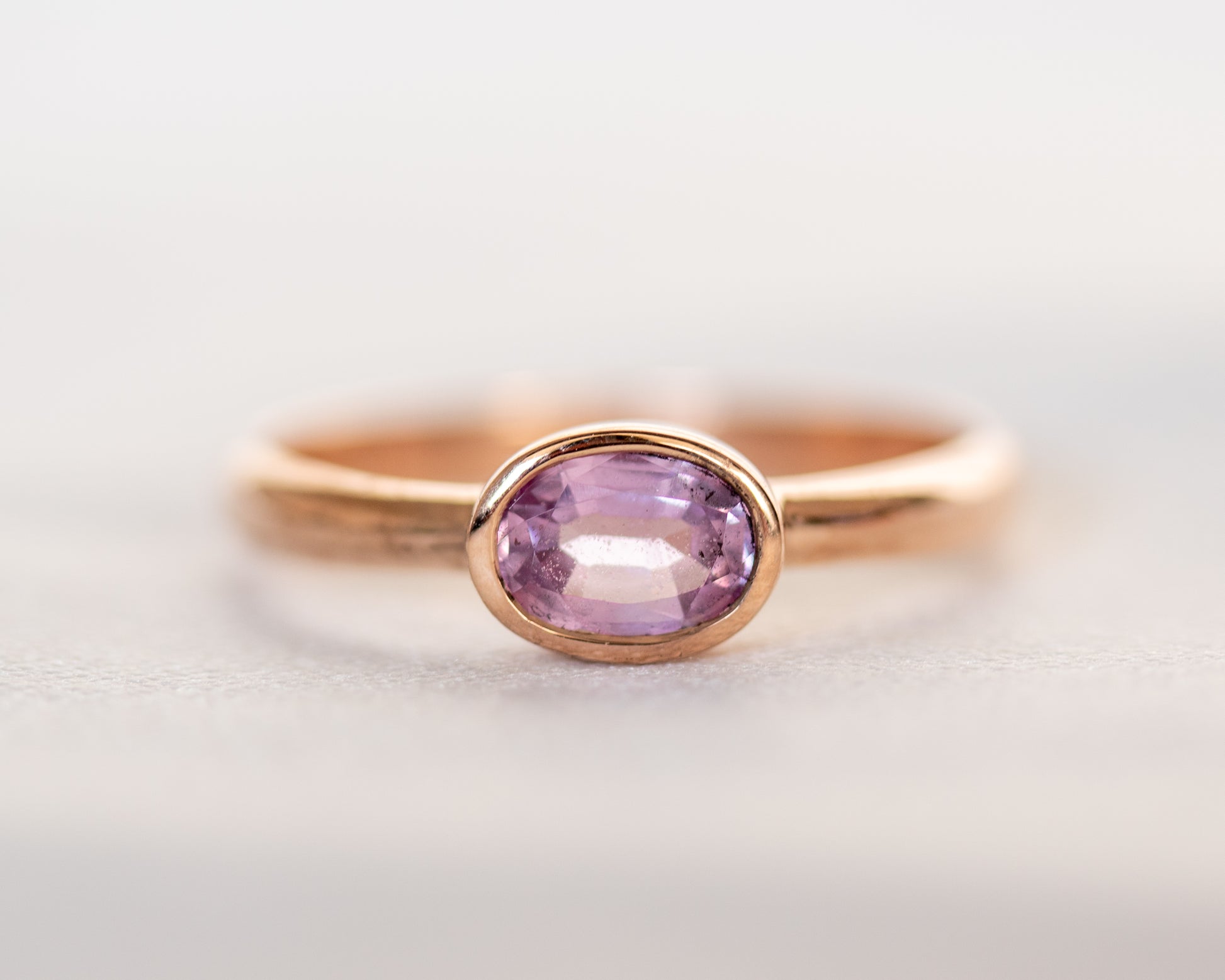 Front view of 14K gold oval pink sapphire ring with full bezel setting