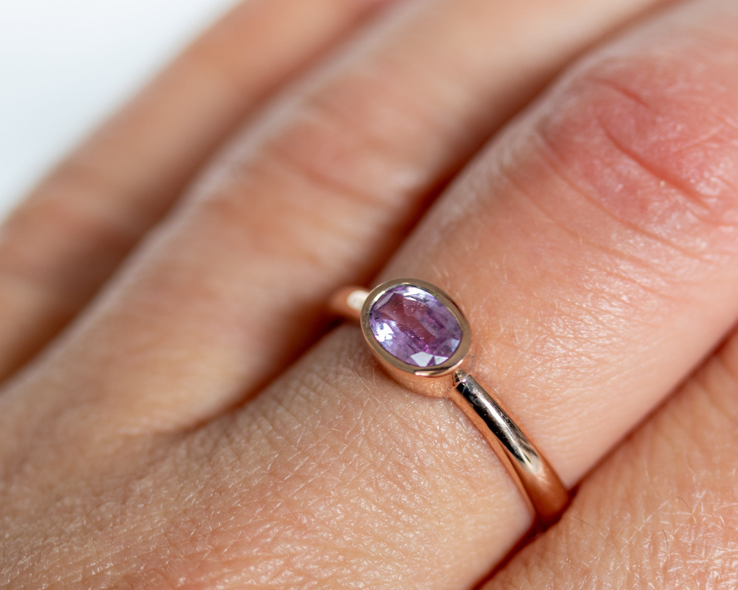 14K rose gold bezel-set oval pink sapphire ring worn on finger