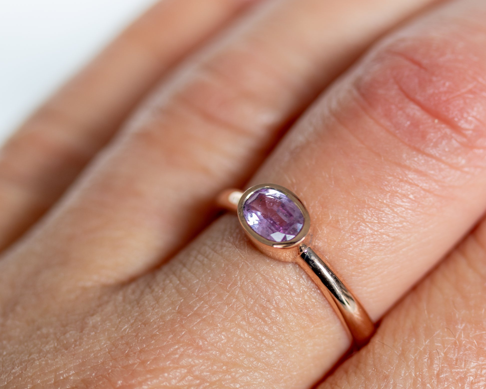 14K rose gold bezel-set oval pink sapphire ring worn on finger