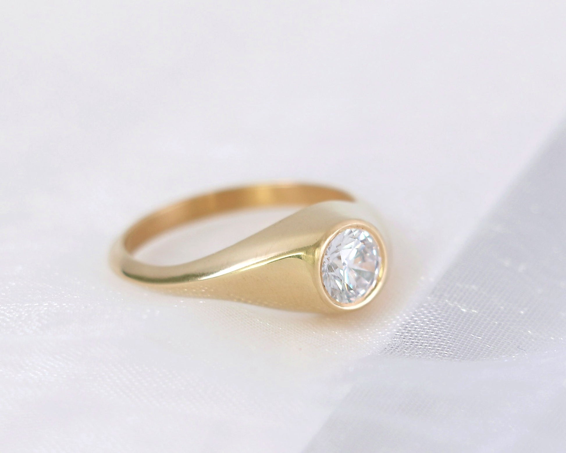 Minimalist 14K gold signet ring with round brilliant diamond, handcrafted fine jewelry with soft cream background and elegant polished finish.