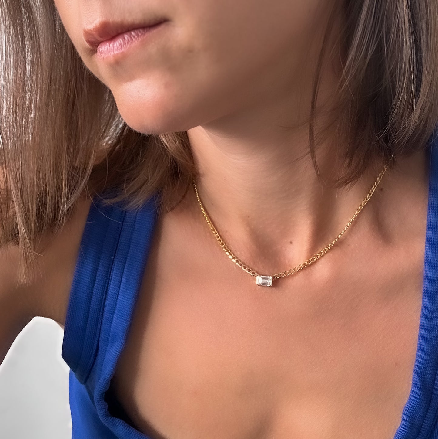 A person wearing a 14K gold diamond solitaire necklace with an emerald cut natural diamond pendant.