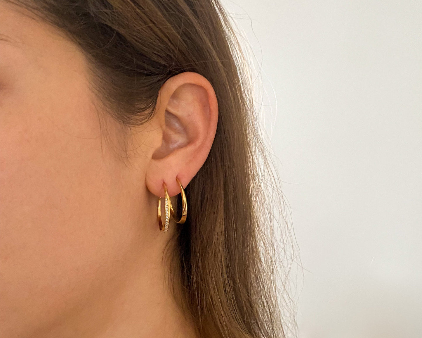 Model wearing 14K gold geometric twist hoop earrings, minimalist sculpted design from the Twist collection, shown on ear to display size and fit.
