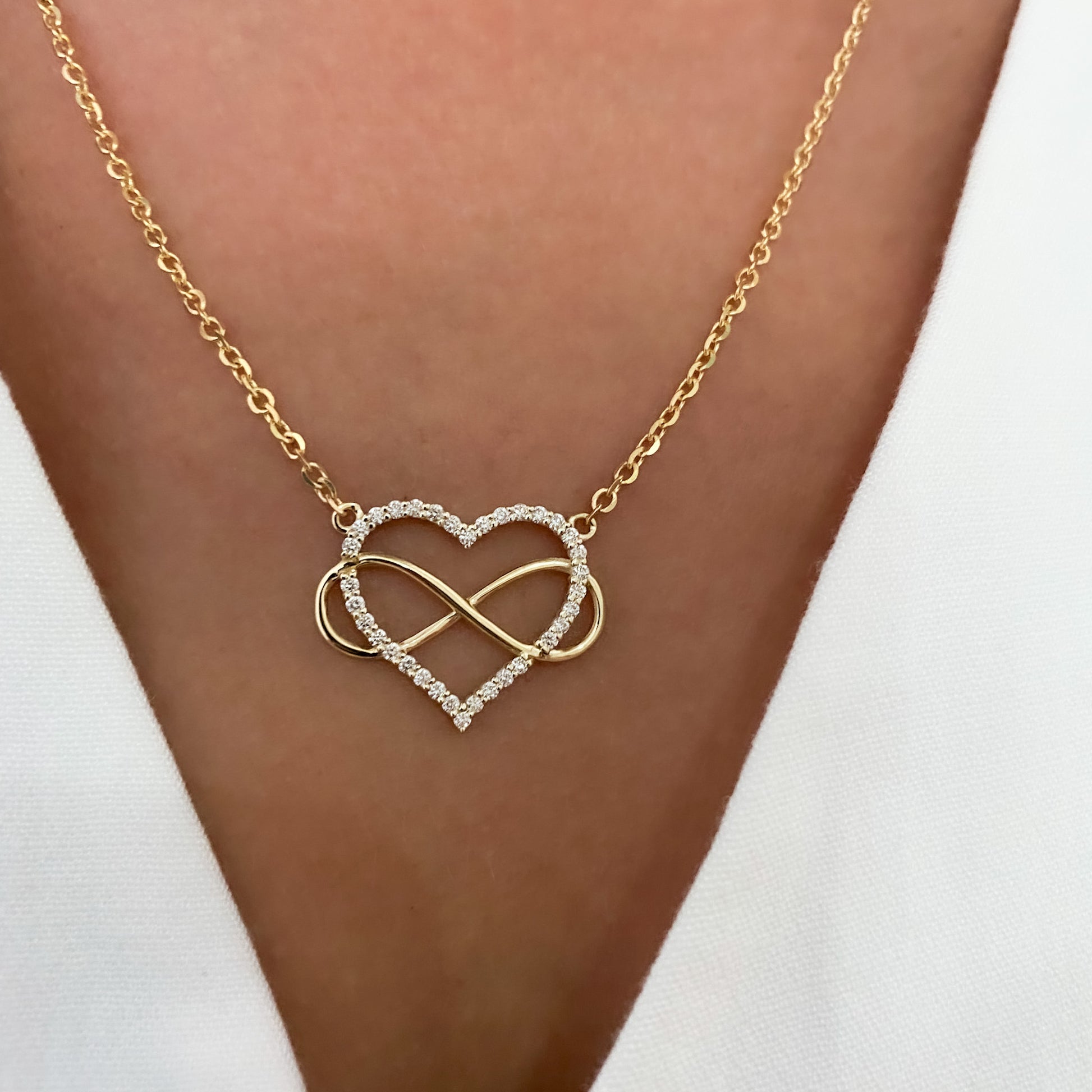 A heart-shaped pendant necklace with a diamonds and gold infinity symbol, attached to a yellow gold chain, displayed on womens neck