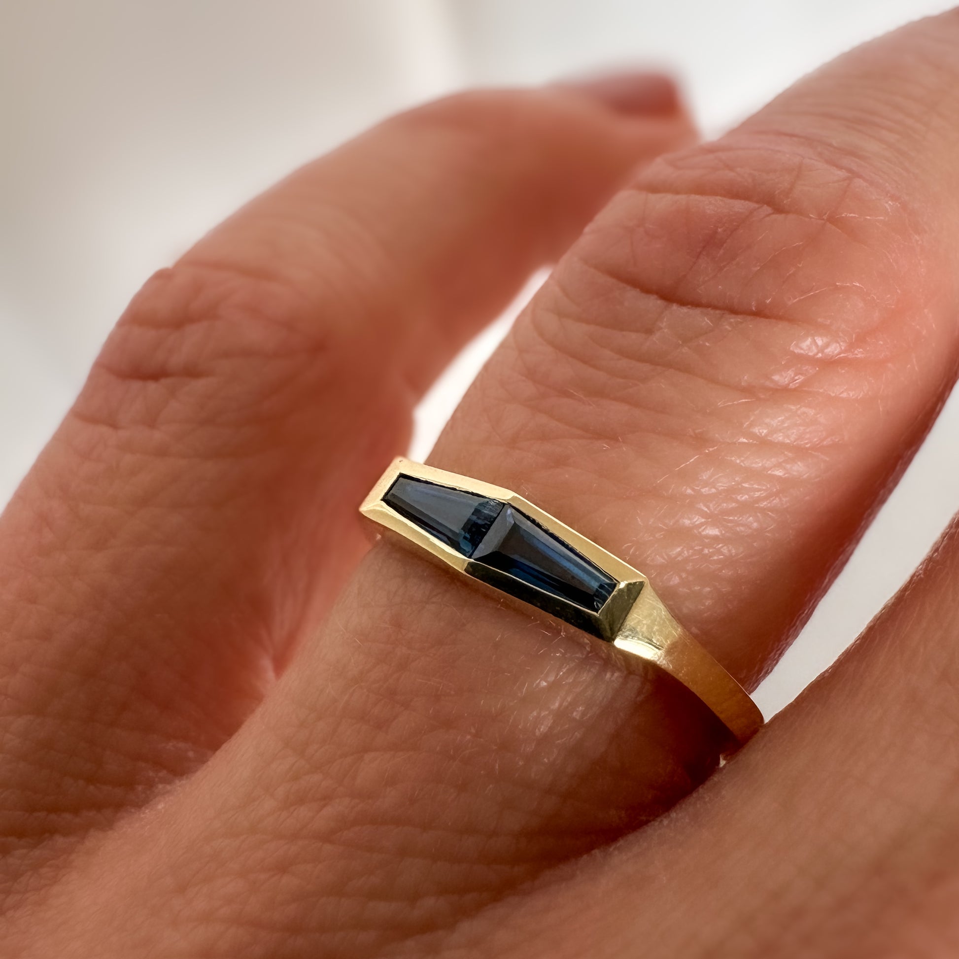 A minimalist gold ring with two blue baguette cut sapphires on finger