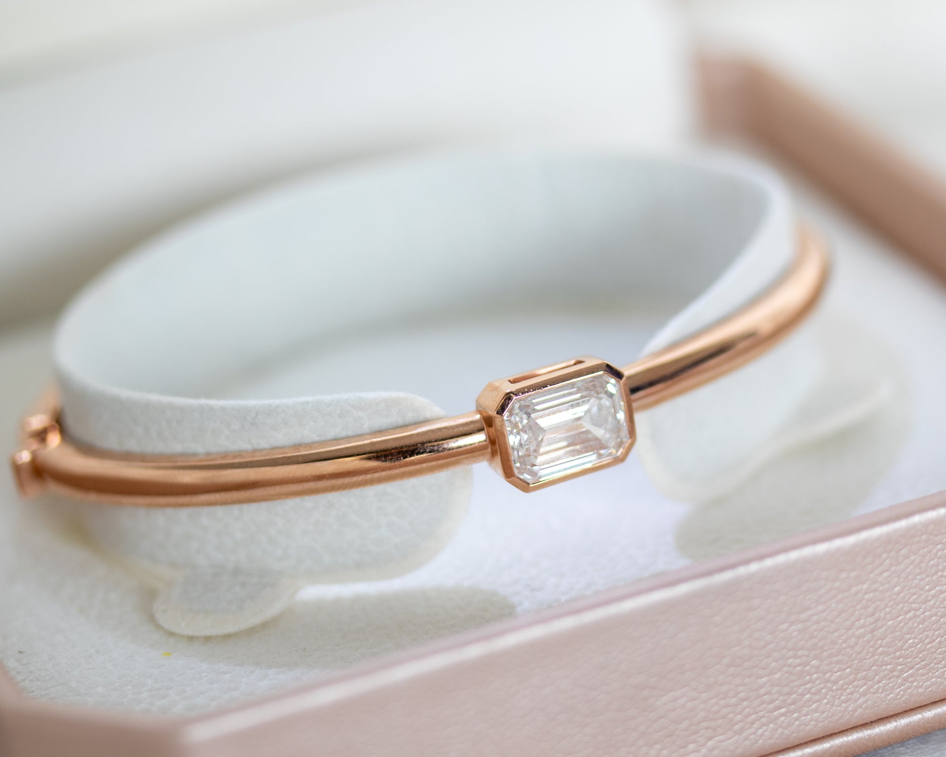14K rose gold emerald cut diamond bangle displayed on a bangle stand inside a jewelry box