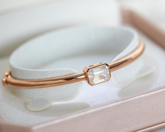 14K rose gold emerald cut diamond bangle displayed on a bangle stand inside a jewelry box