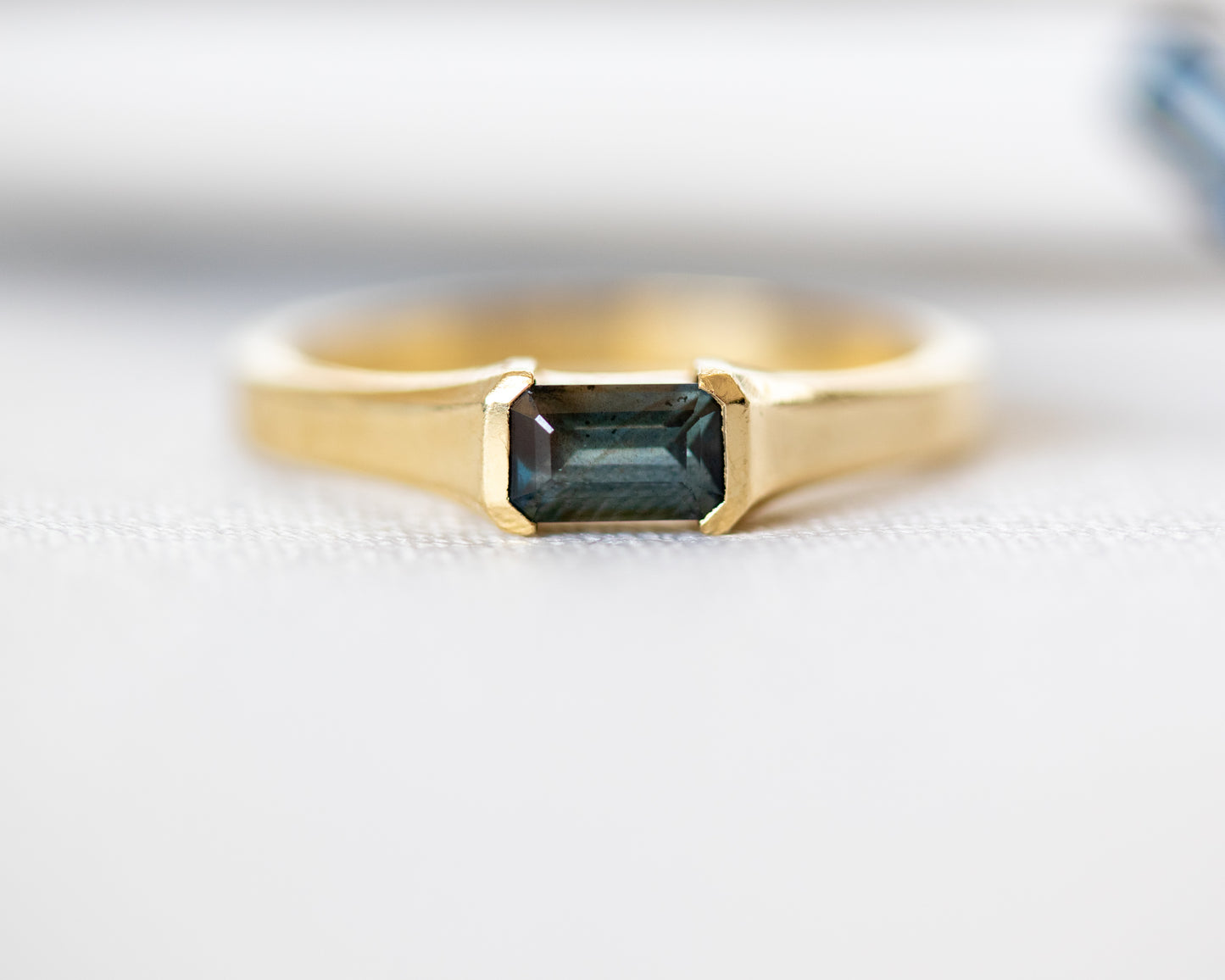 A gold ring with a emerald cut natural sapphire stone, set in a half bezel setting.