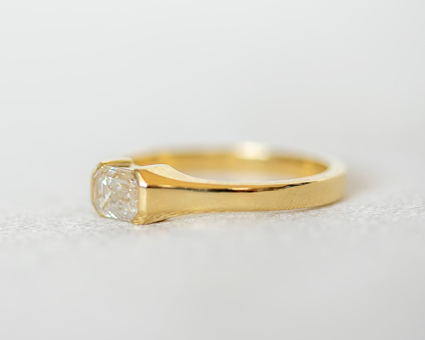 Gold ring with a emerald cut diamond on a light gray background