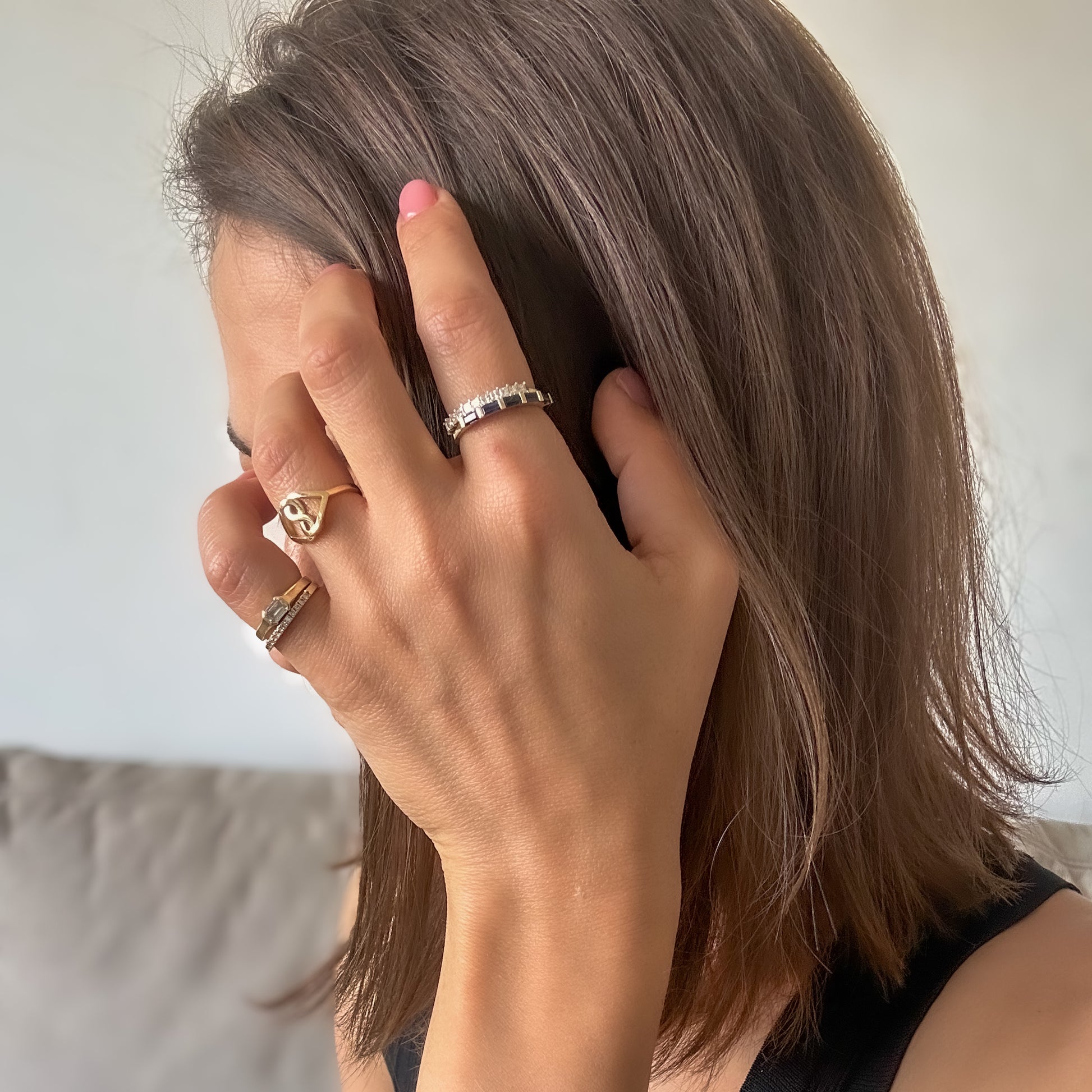 A princess cut natural diamonds eternity ring made from 14K yellow gold stacked with blue sapphire baguette ring on woman's hand while stroking here hair.