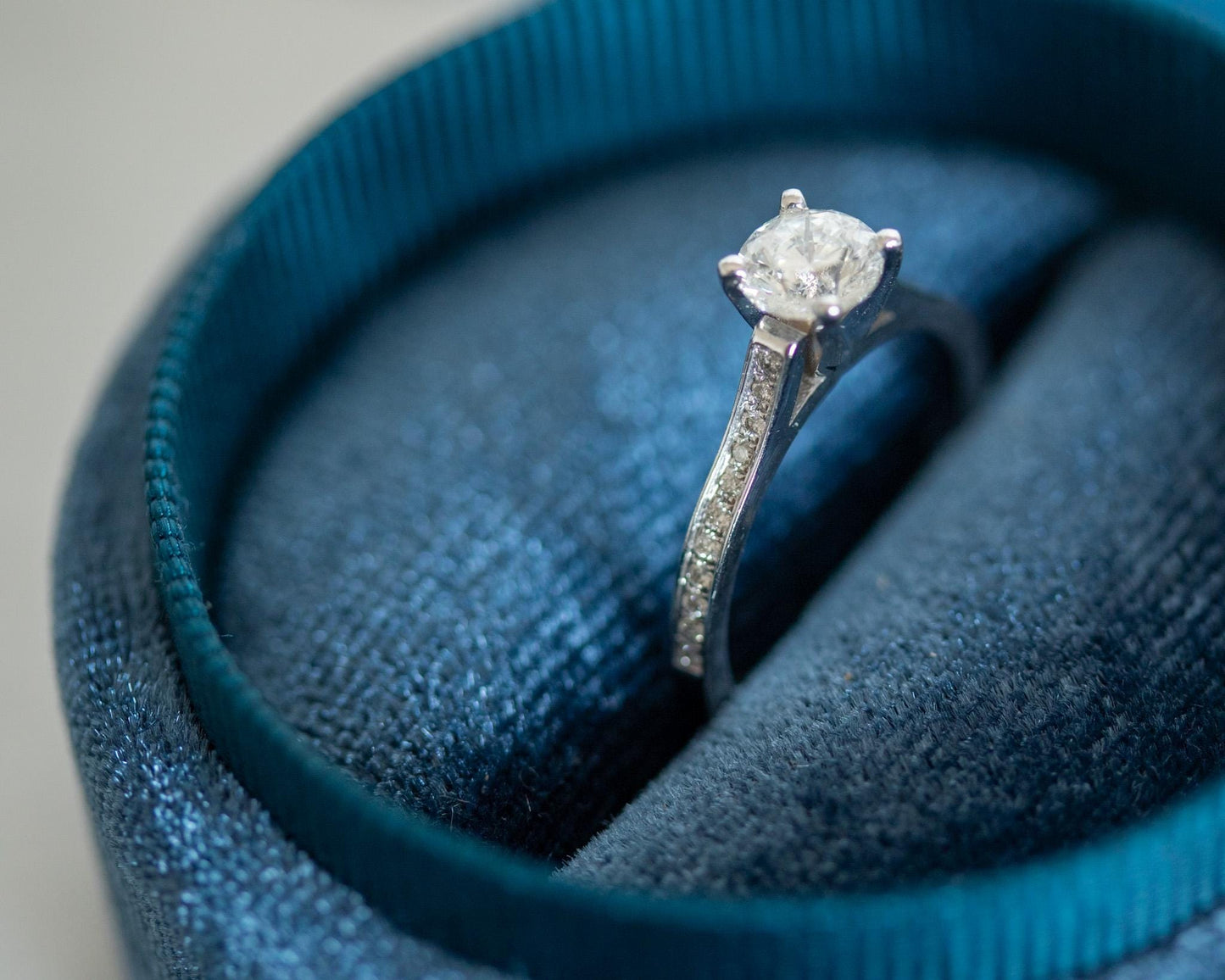 14K white gold engagement ring with round brilliant diamond and pavé band, elegant minimalist design displayed in blue jewelry box"