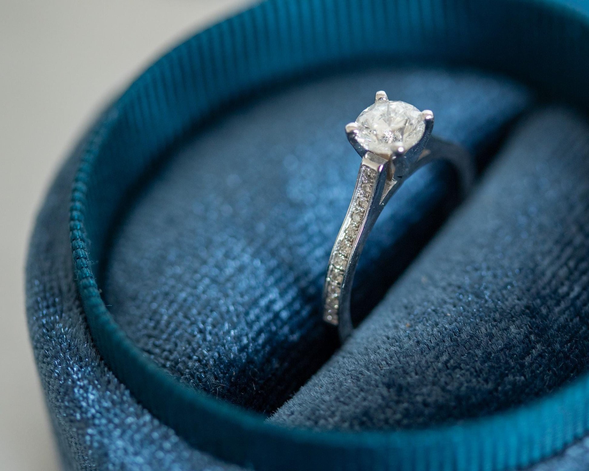 14K white gold engagement ring with round brilliant diamond and pavé band, elegant minimalist design displayed in blue jewelry box"