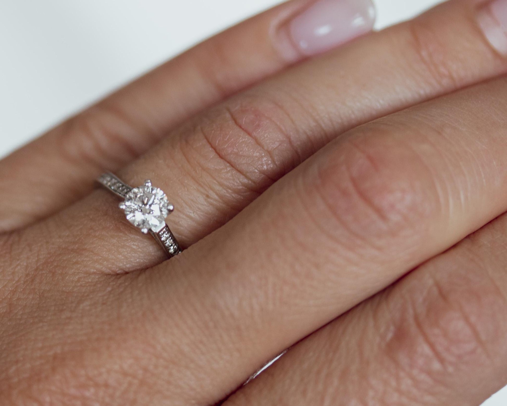 Round brilliant diamond engagement ring in 14K white gold with pavé band, shown on hand for scale and elegant fit