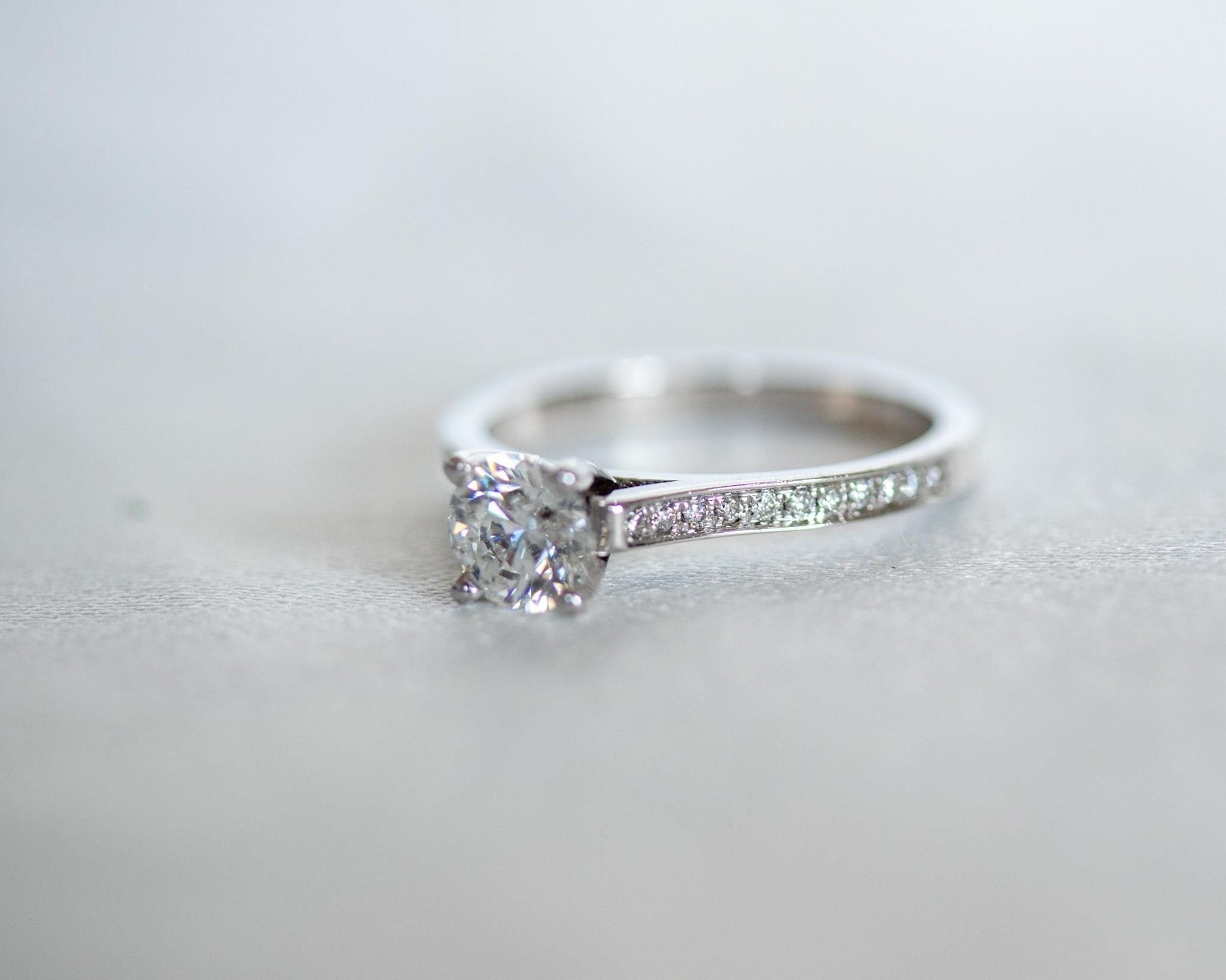 14K white gold engagement ring with round brilliant diamond and pavé band, modern minimalist solitaire on light background