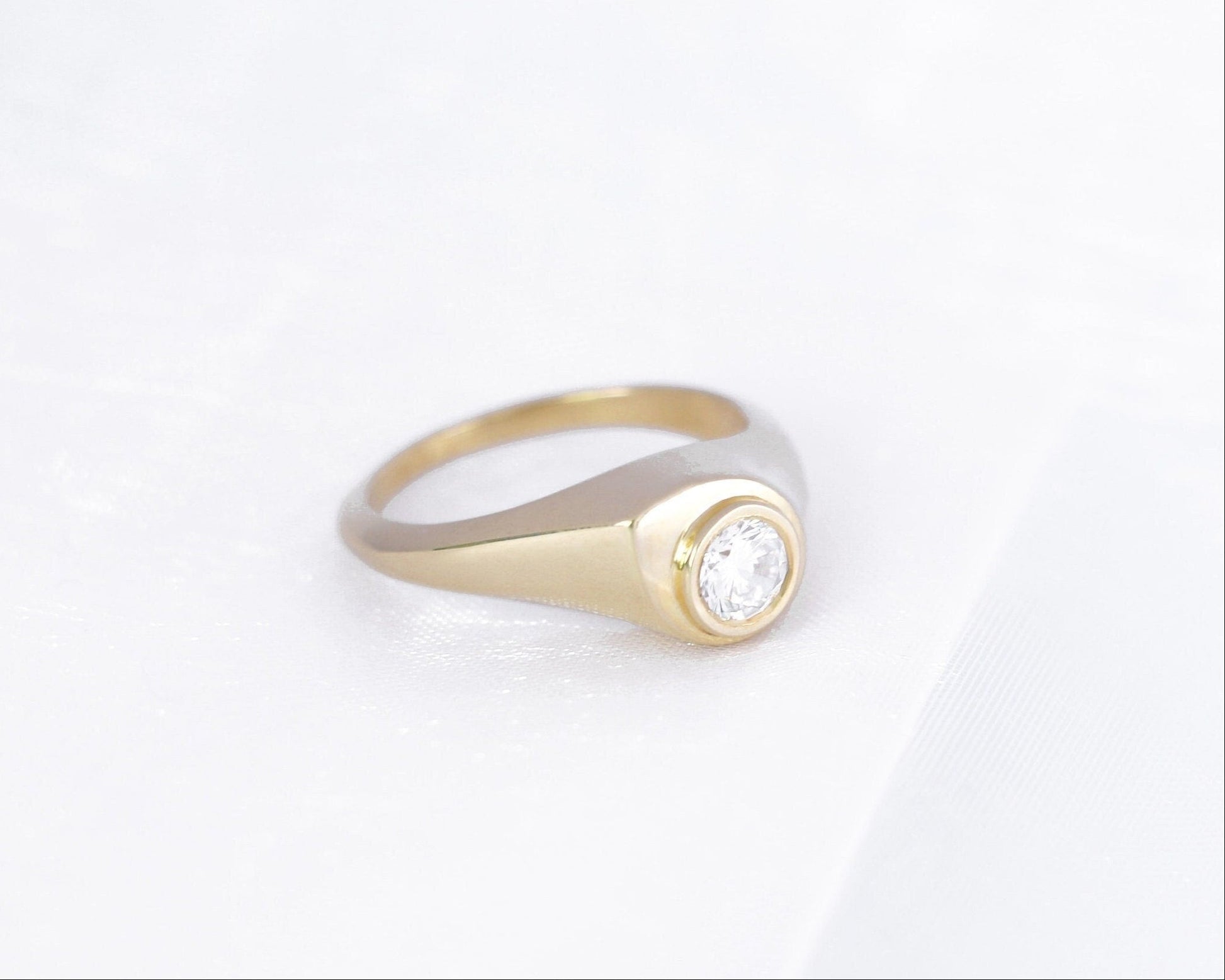 14K yellow gold bezel-set diamond signet ring on a soft white background