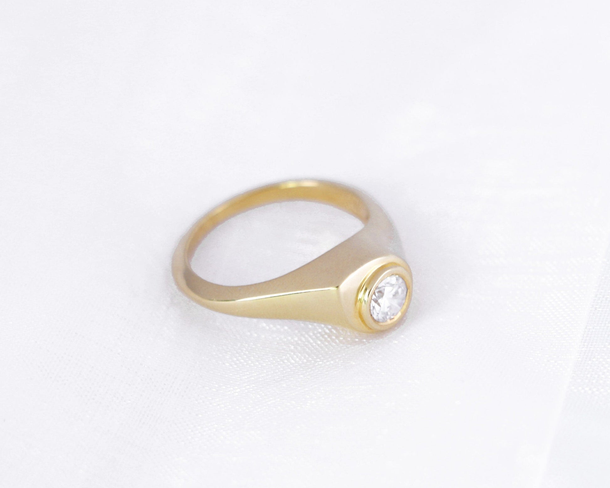 Side view of a 14K yellow gold bezel-set round diamond signet ring on a soft white background