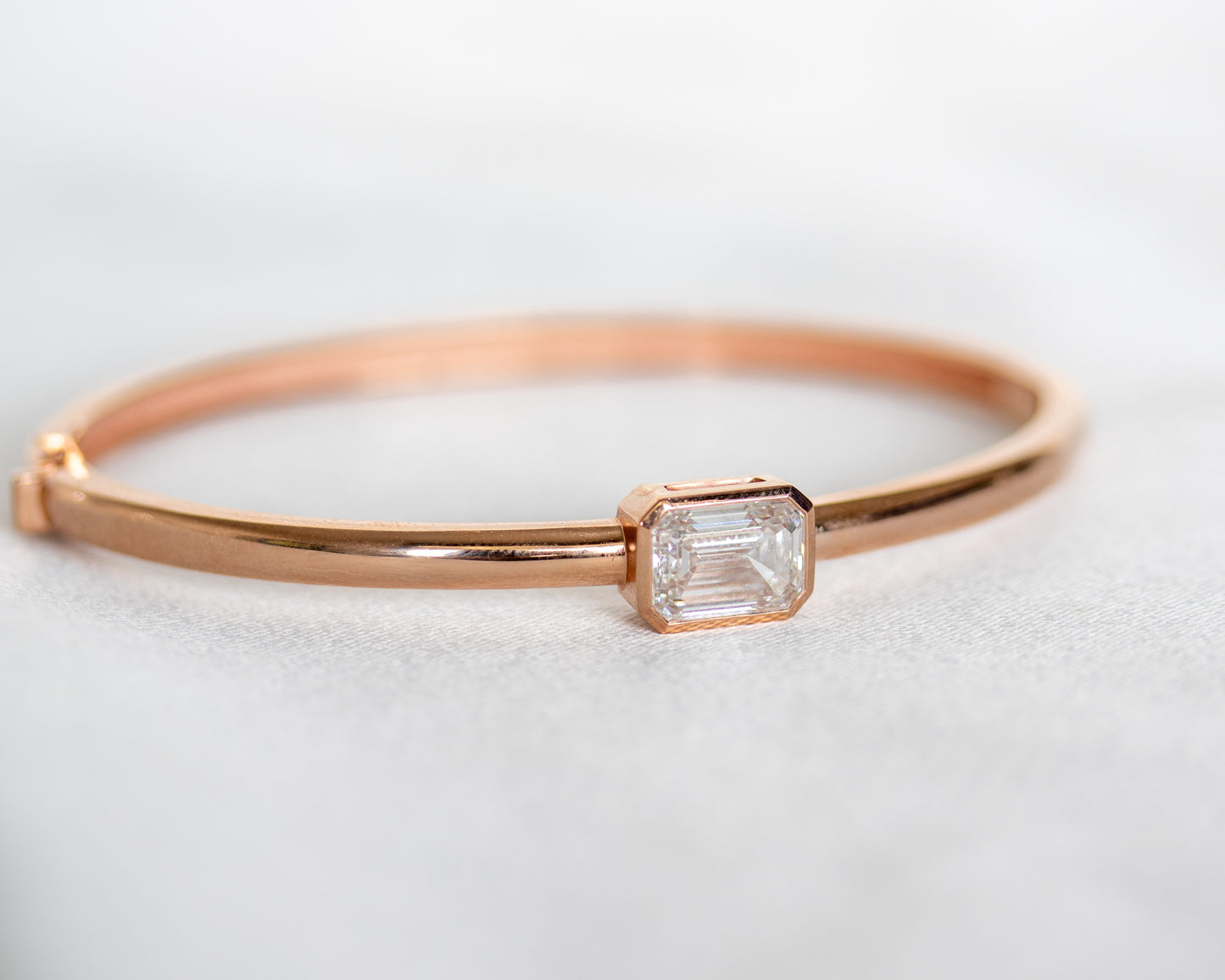 14K rose gold bangle with bezel-set emerald cut diamond, front view on white background