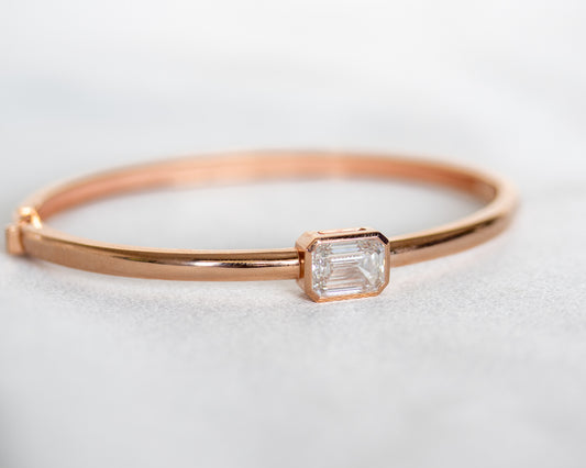 14K rose gold bangle with bezel-set emerald cut diamond, front view on white background